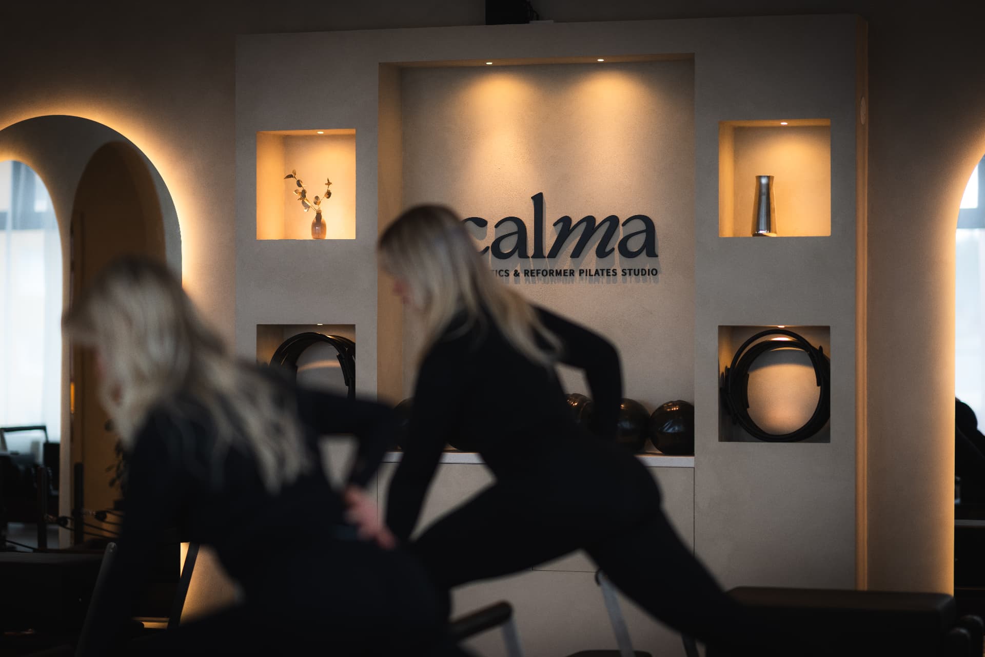 Ljust reformer-pilatesstudio med calma-logotyp på väggen